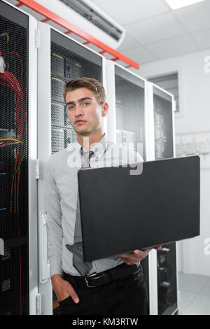 Portrait of modern young man holding laptop standing in server room working with supercomputer Stock Photo