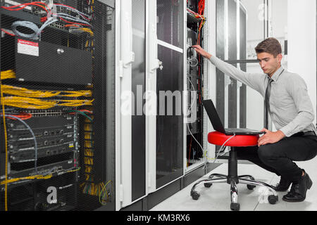 Portrait of modern young man holding laptop standing in server room working with supercomputer Stock Photo