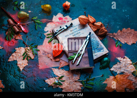 Rainy autumn still life with books, fallen leaves, drawing compasses, papers and water drops on a stone background Stock Photo