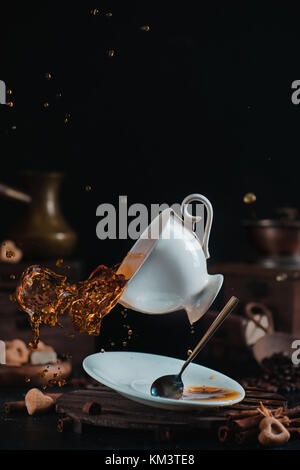 Falling coffee cup with a dynamic splash in a dark scene with cezve, saucer and teaspoon Stock Photo