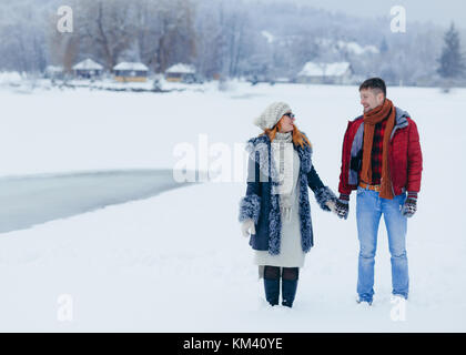 Young happy couple is holding hands and joyfully talking while walking along the snowy countryside. Stock Photo