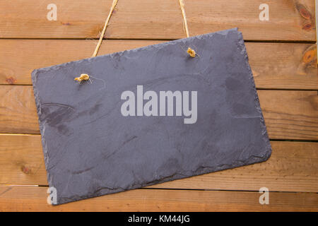 Rustic blank slate noticeboard hanging by twine on a wood background with copy space Stock Photo