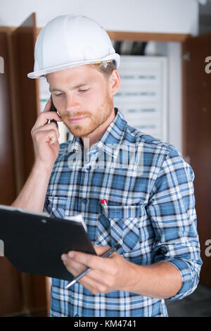 busy construction engineer talking on phone and holding clipboard Stock Photo