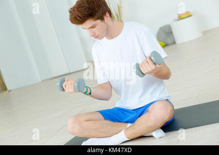 Young man sat on the floor holding weights Stock Photo