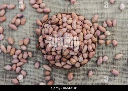 Arachis hypogaea, Raw fresh peanuts in a clay bowl on gunny background Stock Photo