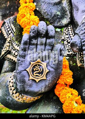 High contrast close up of hand of statue of elephant-headed Hindu god Ganesha (Ganesh) with marigold garland in Ubud, Bali Stock Photo