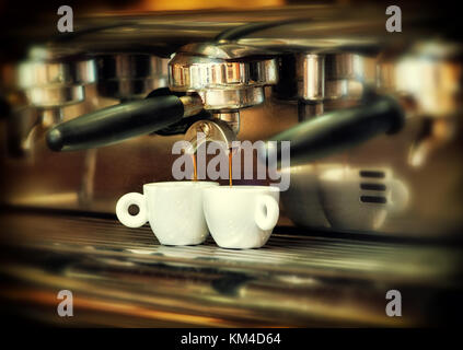 Coffee maker with black handle pours hot coffee into two white ceramic cups. Close-up viewed from the side Stock Photo