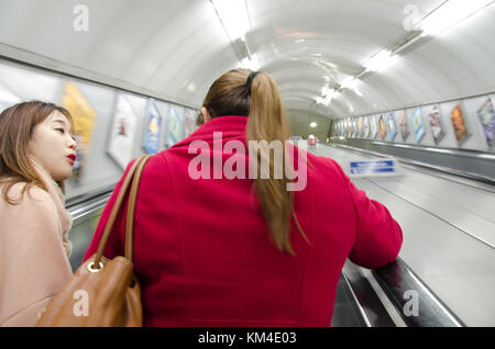 Two friends chat as they go up an escalator on The London Underground. Stock Photo