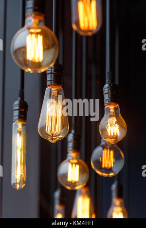 Vintage tungsten filament multiple lamps of different size and style hanging from the ceiling on a black wires as an interior design concept. Energy a Stock Photo