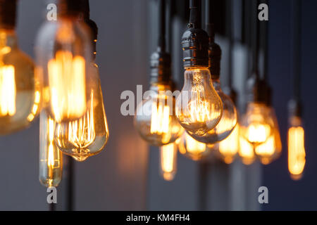 Vintage tungsten filament multiple lamps of different size and style hanging from the ceiling on a black wires as an interior design concept. Energy a Stock Photo