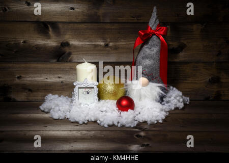 Christmas decoration with candle, picture frame, balls, snow & scandinavian gnome tomte, nisse, tomtenisse, tonttu with ribbon on wooden background. Stock Photo