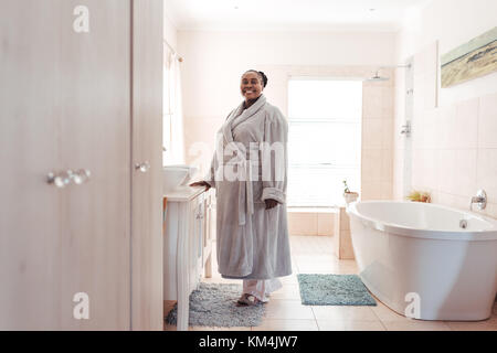 Smiling African woman wearing a robe standing in her bathroom Stock Photo