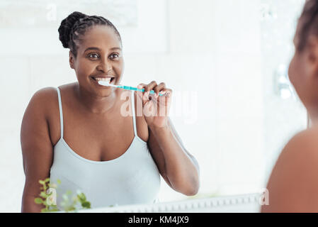 Young African woman brushing her teeth in the bathroom mirror Stock Photo