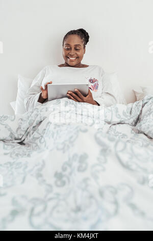 Smiling African woman using a digital tablet in bed Stock Photo