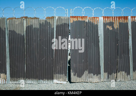 Worn corrugated metal fence, razor wire above. Stock Photo