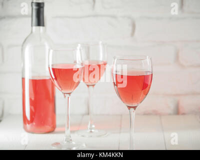 Three wineglass with pink wine and bottle on white brick wall background Stock Photo