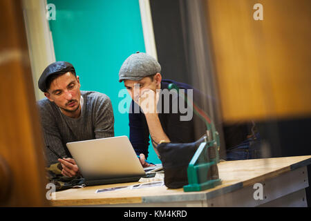 Two men in a tailoring workshop looking at a laptop screen. Stock Photo