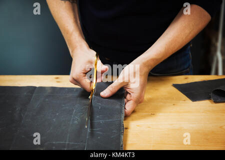 A man cutting a piece of grey fabric with shears. Stock Photo