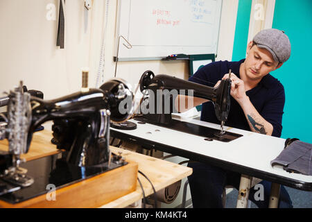 A retro style traditional sewing machine with chased metalwork, and a tailor working in the background. Stock Photo