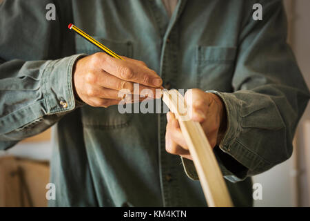 A craftsman using a pencil and marking a piece of curved wood. Stock Photo