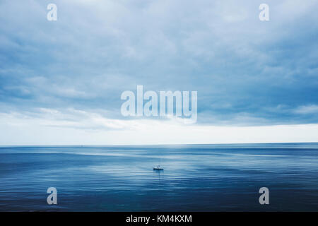 View across a calm sea to the horizon and a cloudy sky. A small yacht, day boat under motor power. Stock Photo