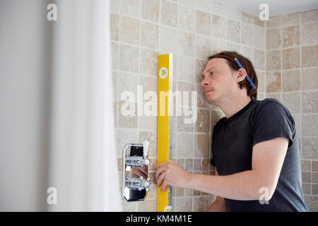 A builder using a spirit level to check his work on a wall of tiles, refurbushing a bathroom. Stock Photo