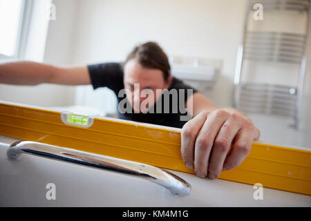 A builder using a spirit level to check his work, refurbushing a bathroom. Stock Photo
