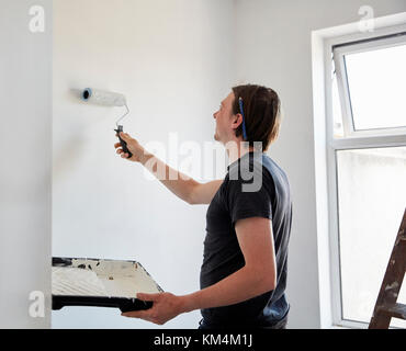 A painter and decorator using a paint roller and holding a paint tray, decorating a room. Stock Photo