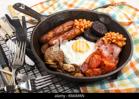full irish breakfast with fried egg, sausages, black pudding, white pudding, baked beans, bacon, tomato and grilled mushrooms in a cast iron pan Stock Photo