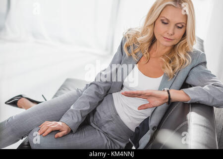 concentrated mature businesswoman looking at watch while waiting for meeting Stock Photo
