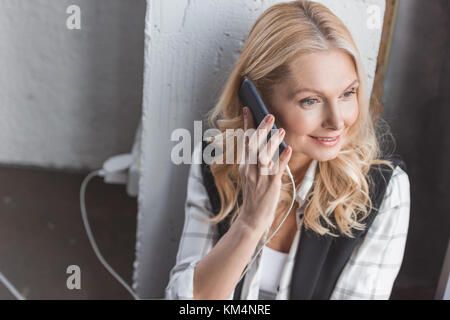high angle view of businesswoman charging smartphone and making call while sitting on floor in office Stock Photo