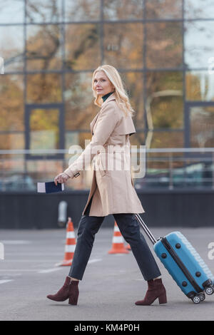 stylish mature woman with suitcase and flight ticket walking by parking Stock Photo