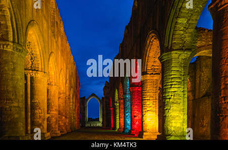 Arched buttresses picked out in colourful lights at dusk in the ancient ruins of Fountains Abbey during Christmas season in Yorkshire, UK. Stock Photo