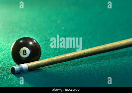 Horizontal photo of a green billiard table and the eight billiard ball next to the stick Stock Photo