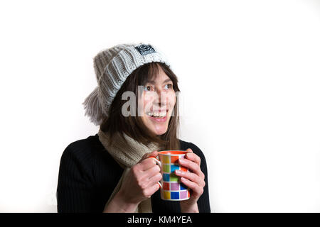 Inside portrait of happy caucasian female isolated in beanie bobble hat, warming hands on mug. Nice big natural smile. Stock Photo