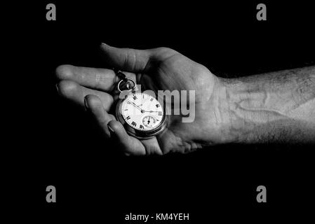 Black & white close up of isolated male hand holding gentleman's old, vintage pocket watch, black background. Out of time, time's up, time out concept. Stock Photo