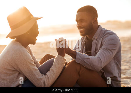 Young African couple sitting together on a beach at sunset Stock Photo