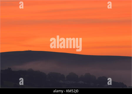 A colorful and orange streaked summer sunrise over Codden hill, Bishops Tawton, Barnstaple, Devon, UK. Mist can be seen forming in the valley below. Stock Photo