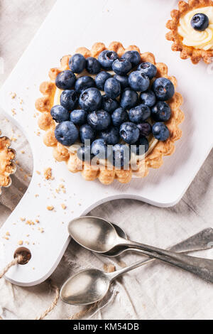 Top view on blueberry mini tart served on white cutting board with vintage teaspoons. Stock Photo