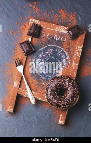 Top view on chocolate and drawing donuts with dark chocolate and dessert fork served on chalkboard over black stone table. See series Stock Photo
