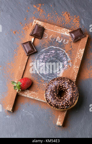 Top view on chocolate and drawing donuts with fresh strawberries and dark chocolate served on chalkboard over black stone table. See series Stock Photo