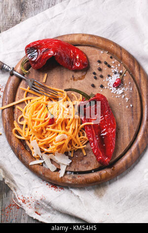 Top view on orange tomato spaghett (tagliolini al pomodoro) with grilled red paprika and cheese parmesan served on wooden cutting board Stock Photo