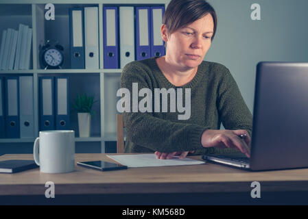 Female freelancer working overtime in home office, doing paperwork and accounting, writing notes and calculating budget Stock Photo