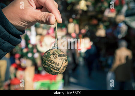 closeup of a young man holding a christmas ball wrapped on pieces of a US 100 dollar bill in a christmas market Stock Photo