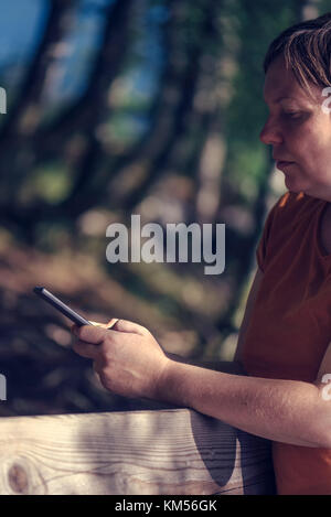Pregnant woman texting outdoors on park bench, adult caucasian female using mobile phone during pregnancy Stock Photo