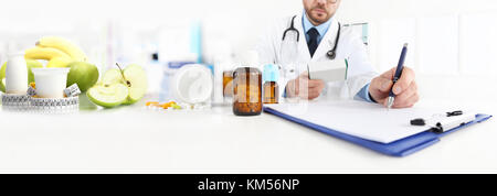 Nutritionist doctor writes the medical prescription for a correct diet on a desk with fruits, drugs and supplements, web banner and copy space templat Stock Photo