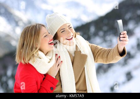 Two happy friends taking selfies in winter holidays with a snowy mountain in the background Stock Photo