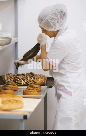 Adult woman in uniform bakes cakes in the bakery Stock Photo