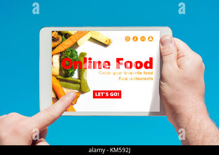 Man holding a tablet device visiting an online food website and touching the screen with a finger with blue sky in background. Stock Photo