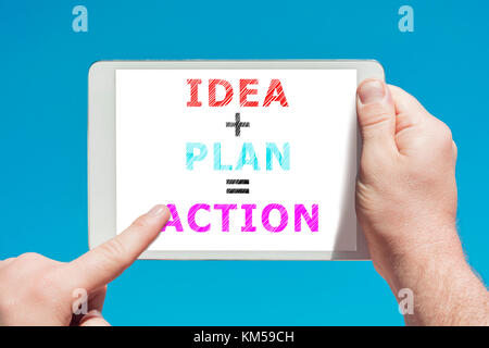 Man holding a tablet device with text idea plan action on the screen and touching it with a finger with blue sky in background. Stock Photo
